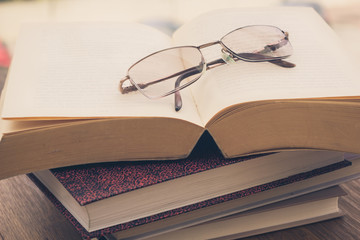 Pile of books and eyeglasses on a wooden table