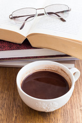 Cup of chocolate on a wooden table with books with books