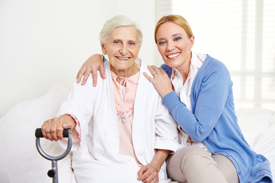 Frau umarmt alte Seniorin zu Hause