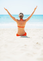 Young woman sitting on beach and rejoicing. rear view