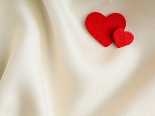 Red wooden decorative hearts on white silk background.