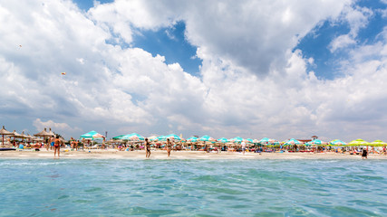 White clouds and blue sky above a crowded sandy beach