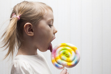 Beautiful little girl eating big colorful lollipop