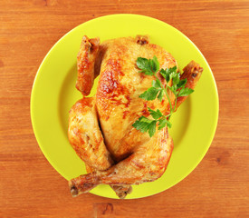 Roasted whole chicken on a green plate on wooden background