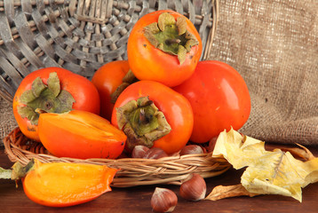 Ripe persimmons with nuts on table on wicker background