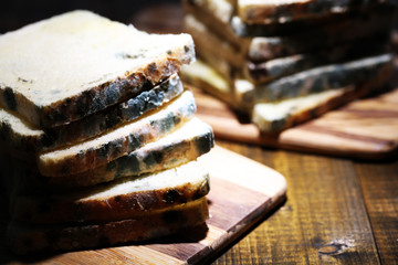 Mouldy bread on cutting board, on wooden background