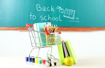 School supplies in supermarket cart on blackboard background