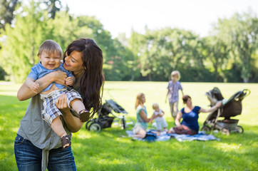 Mother Carrying Cheerful Baby Boy At Park