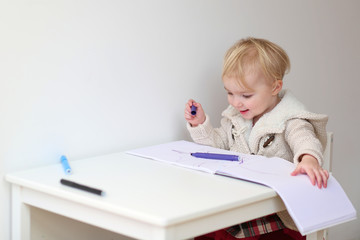 Naklejka premium Happy blonde toddler girl drawing with colorful crayons 