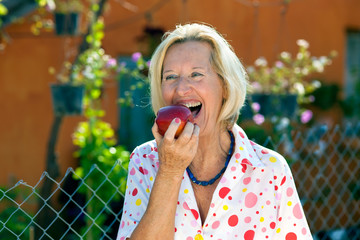 Laughing senior woman eating a red apple.