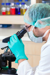 Male lab technician looking down a microscope.
