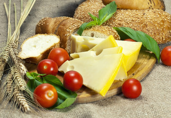 Bread, cherry tomatoes, cheese and basil on wooden cutting board