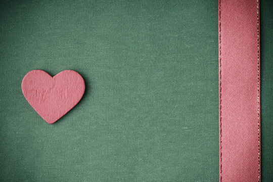 Red wooden decorative heart on green cloth background.