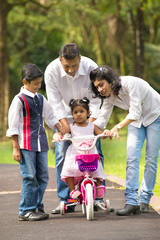 indian family guiding little daughter to cycle