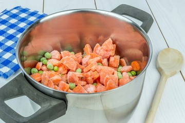 A pot with frozen peas and carrots on the kitchen table