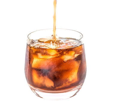 Pouring cola drink into a short glass over white background