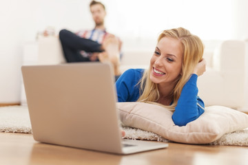 Smiling woman lying down in living room with laptop