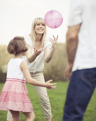 Father mother and daughter throwing ball to each other in the park