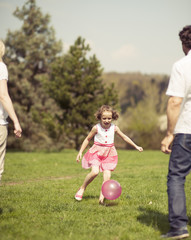 Daughter kicking ball to father and mother in park