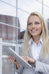 Happy businesswoman using digital tablet while looking away against office building