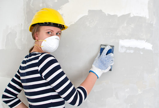 Female plasterer in hard hat polishing the wall.