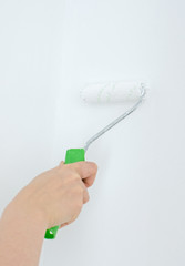 Female hand holding roller with paint on the wall.