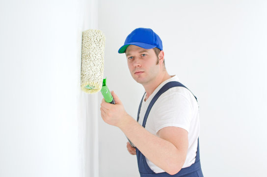 Painter in uniform paints the wall. Focus on roller paint.