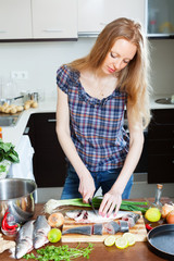Long-haired  woman slicing raw saltwater fish