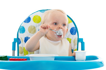 Sweet baby with spoon eats the yogurt.