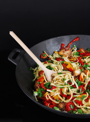 Noodles with vegetables on wok isolated on black