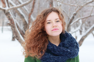 Pretty curly girl in green looks at camera outdoor at winter day