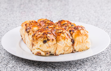 Homemade sweet bun with almond and raisins on a white plate