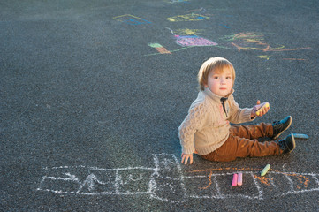 Naklejka premium Cute toddler boy drawing with chalk on a nice day outdoors