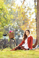 Beautiful young female with bicycle sitting in park