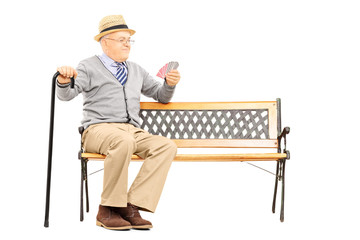 Senile old man with cane, on bench imagining playing cards with