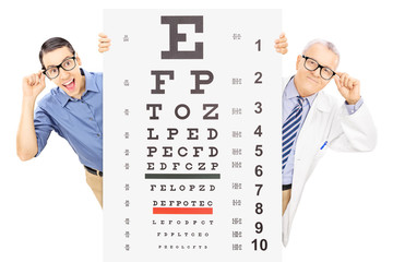 Man and an optician with glasses standing behind eyesight test - obrazy, fototapety, plakaty