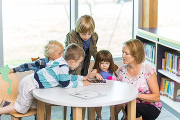 Teacher With Students Using Digital Tablets In Library