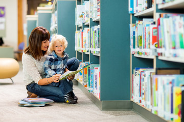 Boy With Teacher Reading Book In Library