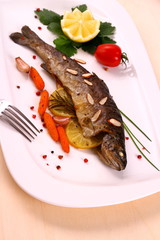 Fried trout with vegetables and split almonds on white plate