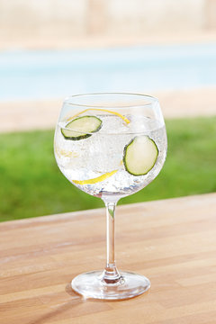 Cucumber gin and tonic cocktail by a pool outdoors