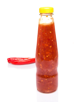 Fresh red chili and bottled chili sauce over white background