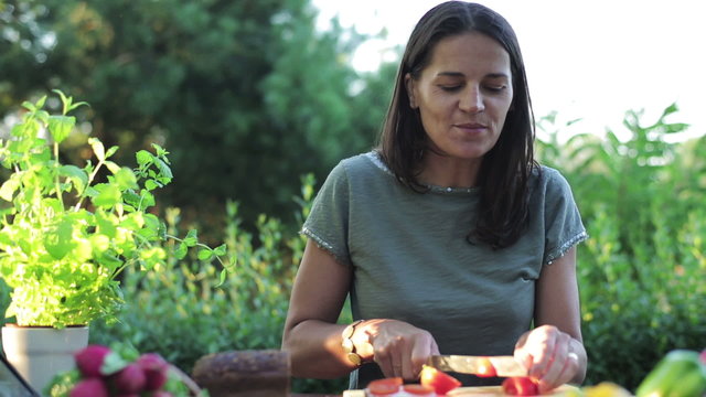 woman cutting tomato by the table in the garden