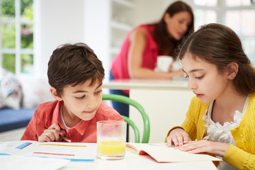 Children Doing Homework As Mother uses Laptop In Background