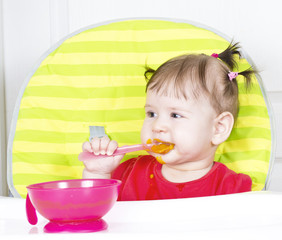 Little baby girl eating a vegetable puree in a highchair