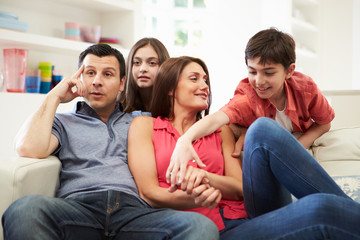 Hispanic Family Sitting On Sofa Watching TV Together