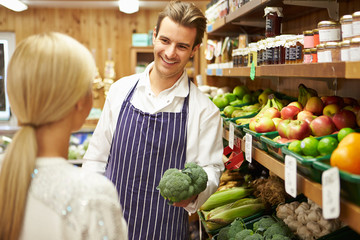 Assistant Helping Customer At Vegetable Counter Of Farm Shop