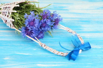 Beautiful bouquet of cornflowers in basket on blue background