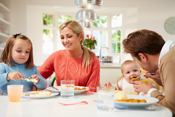 Family With Young Baby Eating Meal At Home