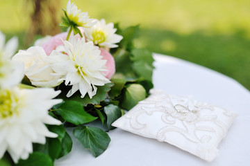 wedding rings on a white pillow near flowers