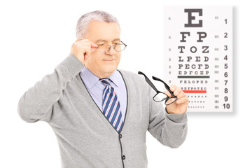 Senior gentleman trying on glasses in front of eyesight test